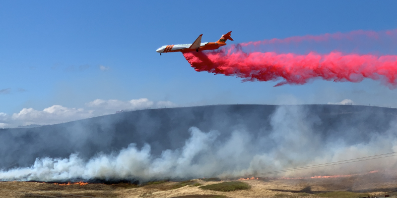 plane spraying fire retardant on forest fire